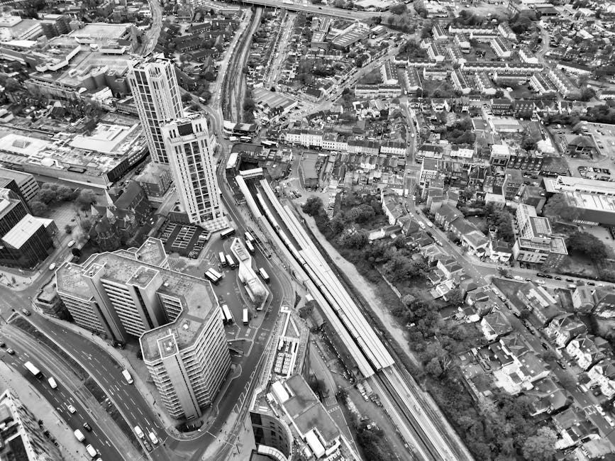 A black-and-white aerial photograph of Hornchurch, showcasing a mix of high-rise office buildings and residential houses. The image features a prominent railway station with train tracks and platforms