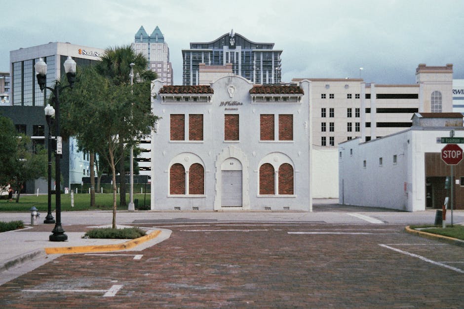 A white two-story building with a rustic, vintage appearance displaying four large red brick arch-shaped windows, a centered white door, and decorative white trim at the top, situated in an urban sett