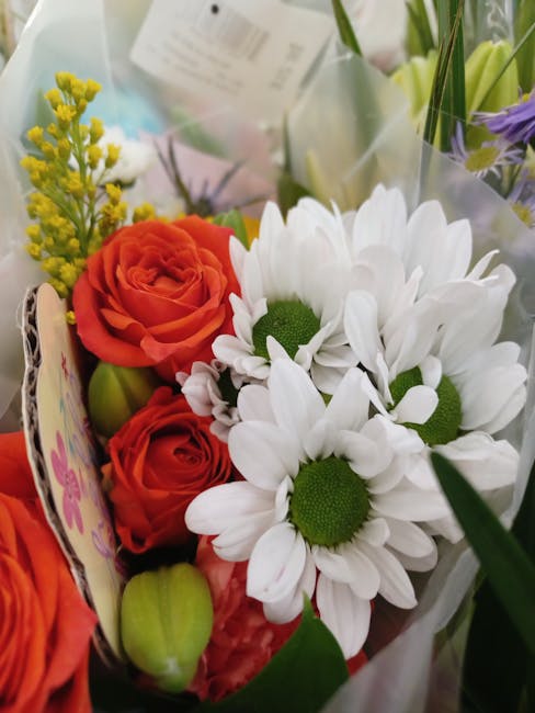 A close-up view of a fresh floral bouquet featuring vibrant orange roses with tightly curled petals, white daisies with bright green centers and delicate petals, and sprigs of small yellow filler flow
