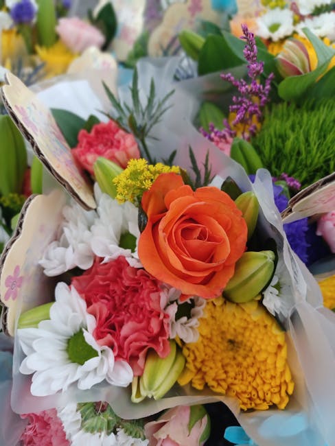 A vibrant floral arrangement featuring a prominent orange rose at the center, surrounded by white daisies with green centers, pink carnations, yellow chrysanthemums, and purple lavender sprigs. The bo
